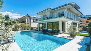 Una casa moderna con piscina, mobiliario exterior y un balcón.
