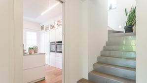 Una escalera conduce a una cocina con armarios blancos y una planta en maceta.