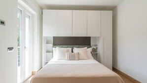 Un dormitorio moderno con una cama grande, cabecera empotrada y puerta corrediza de vidrio que da a un balcón.