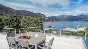 Una terraza con mesa y sillas con vistas a un lago con barcos, rodeada de montañas.