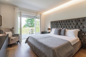 Ein Schlafzimmer mit einem großen Bett, einem Sessel, einem Schreibtisch und Blick ins Freie.