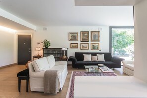 A living room with a white sofa, a black sofa, a glass coffee table, and a fireplace. - Villa Chiara (Stresa)