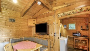 L’intérieur d’un chalet en bois comprend une table à manger, des bancs, un téléviseur, un petit coin cuisine et un panneau décoratif mural.