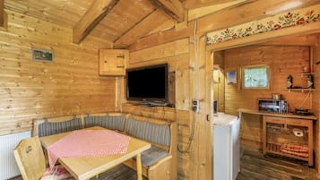 L’intérieur d’un chalet en bois comprend une table à manger, des bancs, un téléviseur, un petit coin cuisine et un panneau décoratif mural.