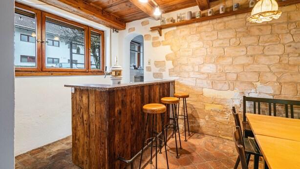 Une cuisine rustique avec un bar en bois, des tabourets et des murs en pierre.