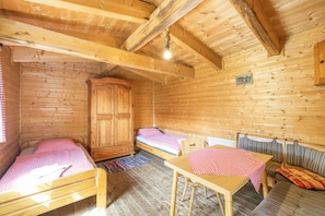 A wooden cabin interior with two beds, a table, a bench, and a wardrobe.