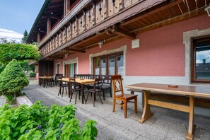 A building with a balcony, wooden furniture, and a small tree.