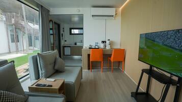 Una habitación de hotel moderna con sofá, televisión, escritorio con sillas, área de cocina y balcón con vistas.
