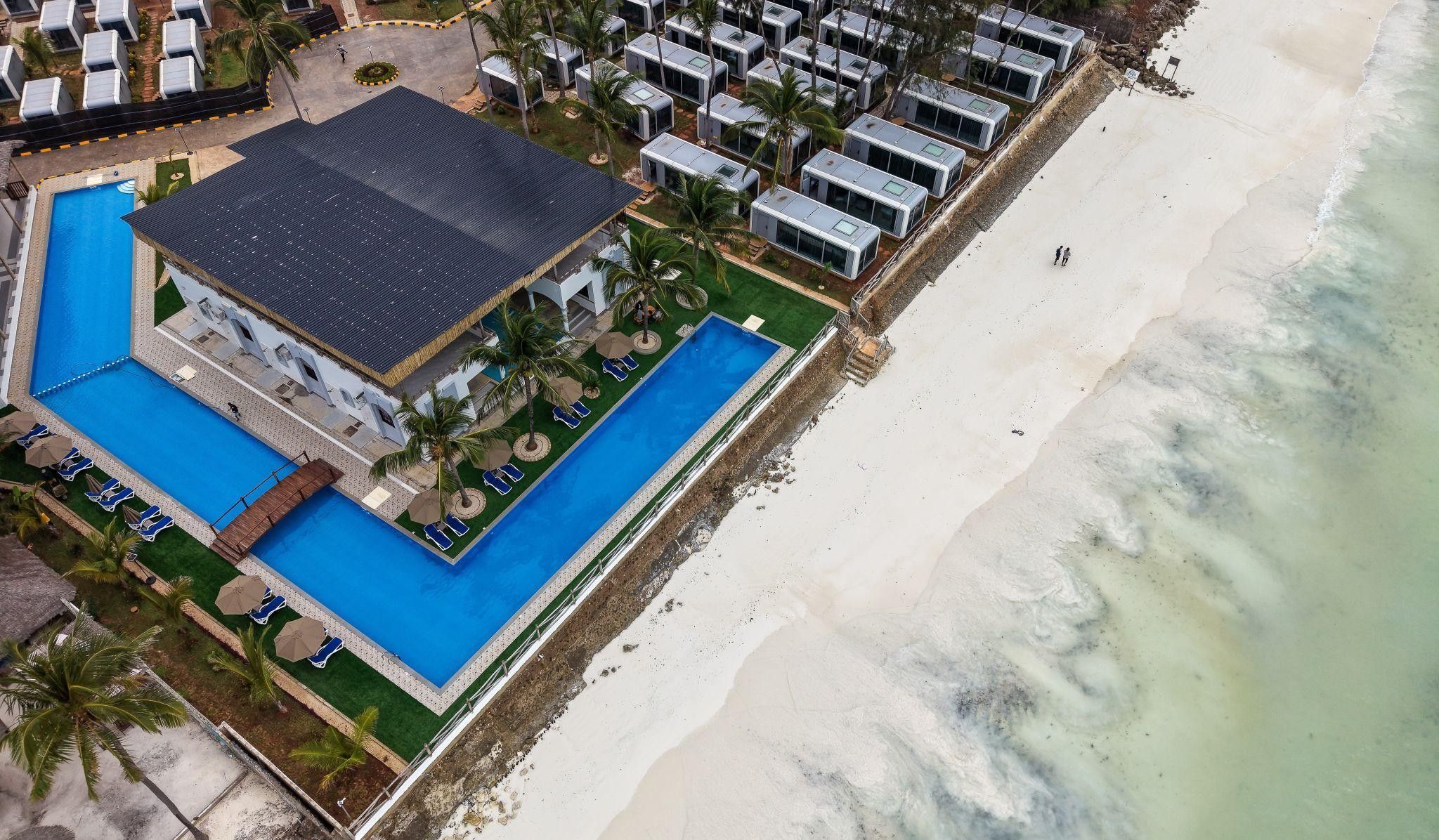 Vue aérienne d’un complexe hôtelier doté d’une grande piscine, de villas en bord de mer et d’une plage de sable.