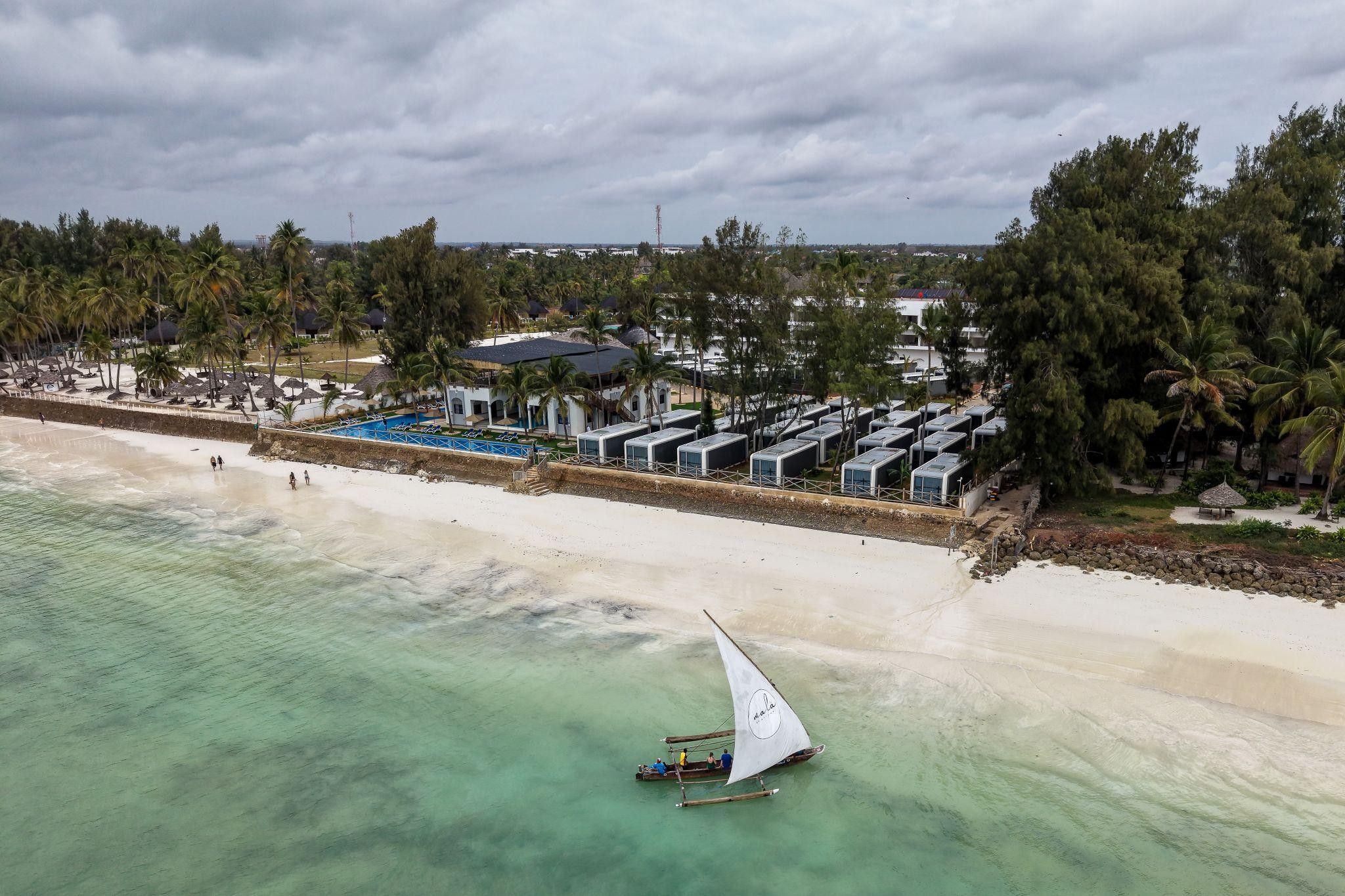 A beachside resort with a swimming pool, beach umbrellas, and a sailboat.