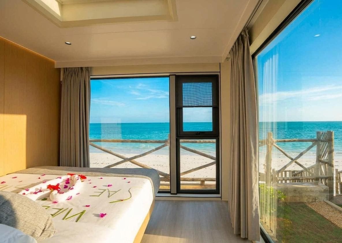 Quarto de hotel com cama, janela grande e vista para a praia.
