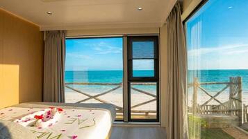 Quarto de hotel com cama, janela grande e vista para a praia.