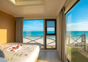 A hotel room with a bed, a large window, and a view of the beach. - Sea Side Resort (Paje)