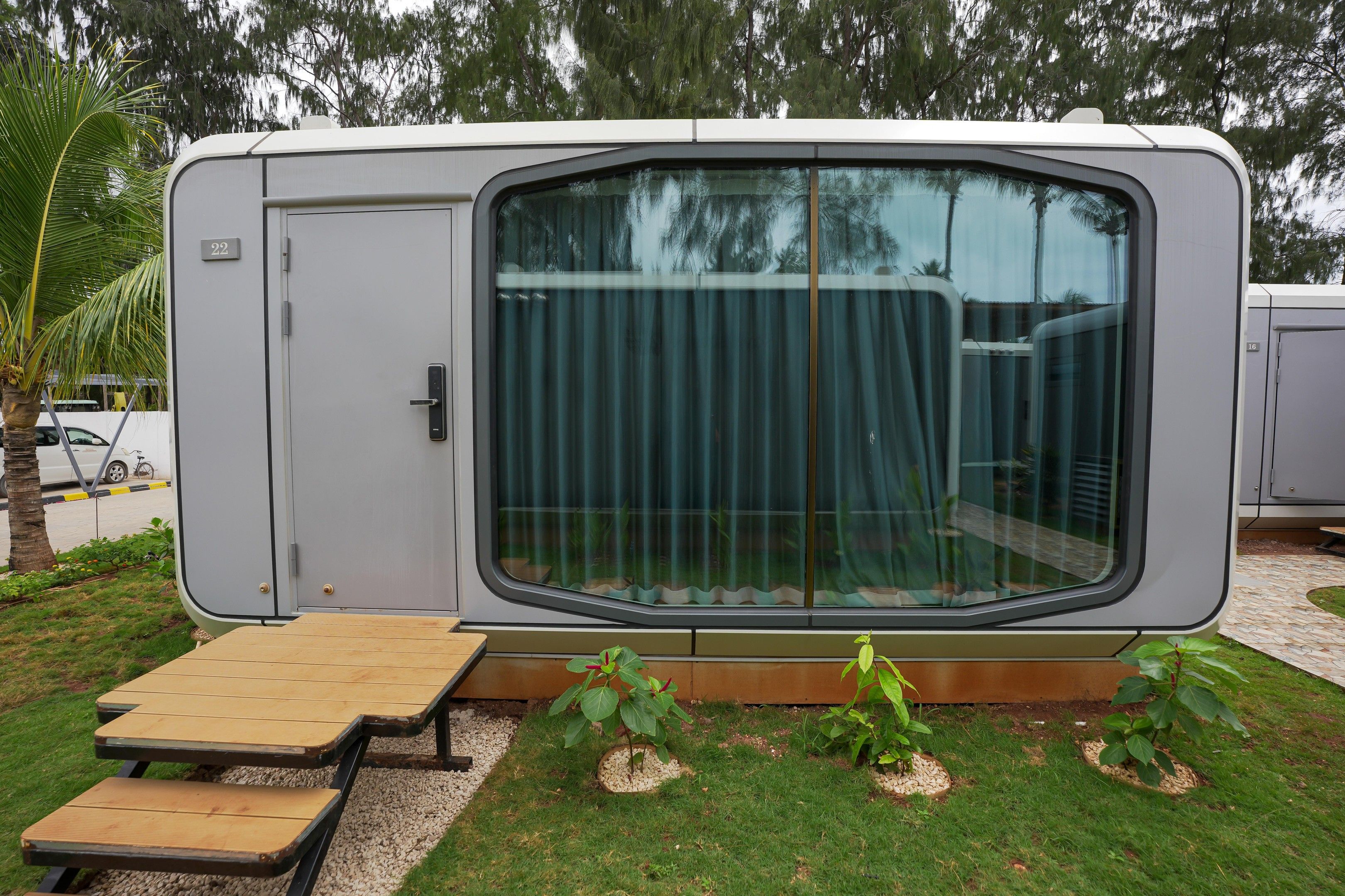 Una autocaravana moderna con un ventanal grande, una puerta y un pequeño espacio de estar exterior con una mesa y bancos.