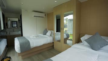 A modern hotel room with two beds, a large mirror, a wardrobe, and a bathroom with a sink and mirror.