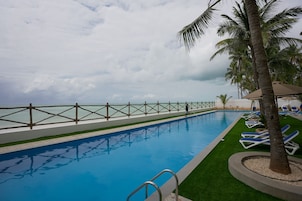A swimming pool with a view of the sea, surrounded by palm trees and lounge chairs.