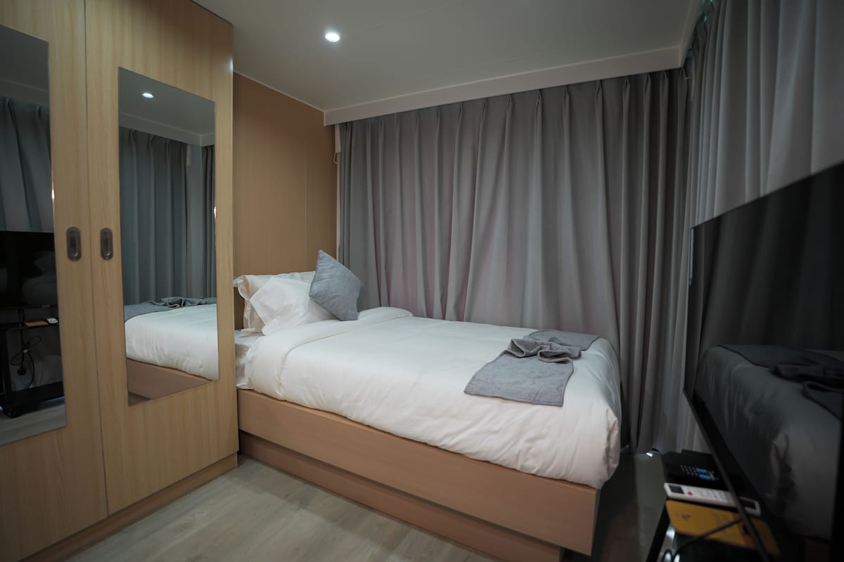 A hotel room with a bed, a TV, a desk with a phone, and a mirror.