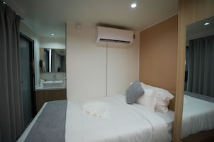 A hotel room with a bed, a bedside table, a mirror, an air conditioning unit, and a bathroom with a sink.