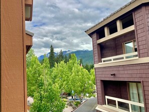 A building with a balcony overlooking a courtyard with trees and a mountain view. - Marketplace Whistler Sensation 2Bdr 2Bath (Whistler)
