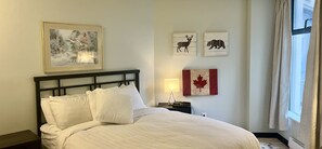 Une chambre d’hôtel comprenant un lit, une table de chevet, une lampe, un tableau encadré représentant un cerf, un tableau encadré représentant un ours et un drapeau canadien encadré.