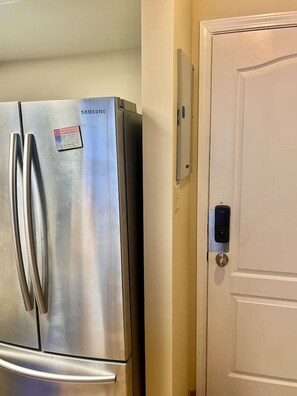 A stainless steel Samsung refrigerator next to a white door with a doorbell. - Marquise Magic Mountain Escape. (Whistler)