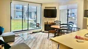 A modern living room with a glass sliding door leading to a patio, a flat-screen TV mounted on the wall, and a dining area with a table and chairs. - Marquise Magic Mountain Escape. (Whistler)
