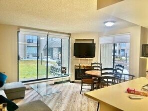 A modern living room with a glass sliding door leading to a patio, a flat-screen TV mounted on the wall, and a dining area with a table and chairs. - Marquise Magic Mountain Escape. (Whistler)