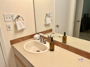 Une salle de bain d’hôtel équipée d’un lavabo, d’un miroir, d’un porte-serviettes et d’un flacon de savon liquide.