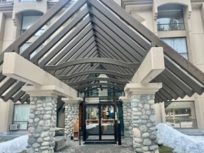 A hotel entrance with a stone facade, a glass door, and a covered entrance area. - Marquise Magic Mountain Escape. (Whistler)