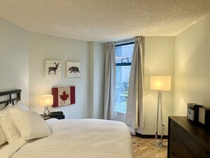 A hotel room with a bed, a nightstand, a lamp, a dresser, and a window with curtains. - Marquise Magic Mountain Escape. (Whistler)