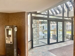 En betalautomat för parkering och en entré med glasväggar och en mur av sten.