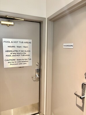 A door with a sign indicating pool and hot tub areas, operating hours, a no-glass policy, and a caution about icy stairs. - Whistler Serenity Sanctuary (Whistler)