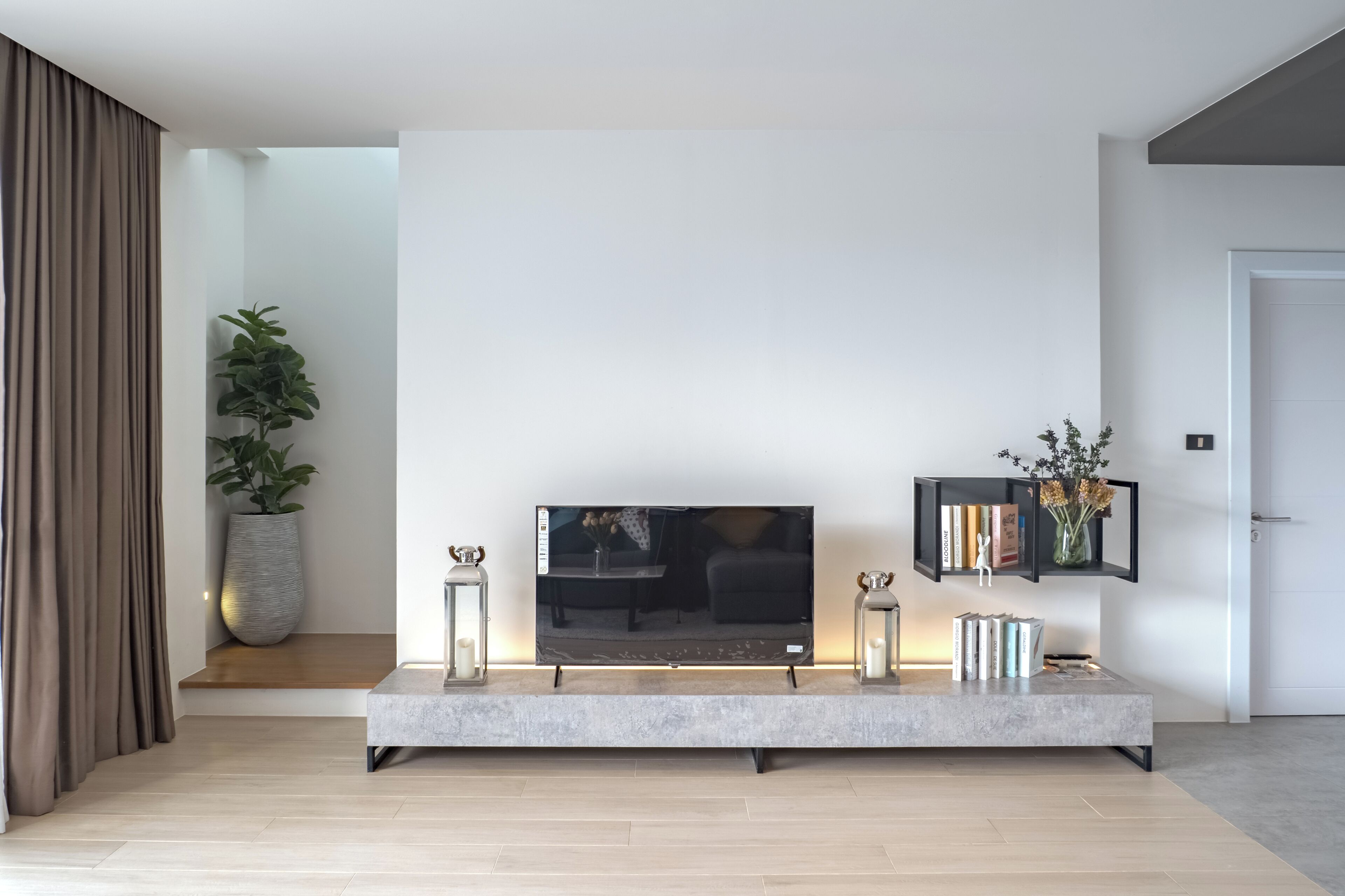 Un salon moderne avec un téléviseur à écran plat posé sur un meuble minimaliste, une plante en pot et une bibliothèque contenant des livres et des objets décoratifs.