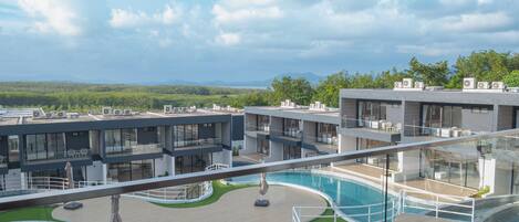 A modern hotel with a rooftop pool, multiple balconies, and a view of the surrounding landscape.