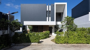 A modern two-story building with a flat roof, large windows, and a concrete pathway leading to the entrance.