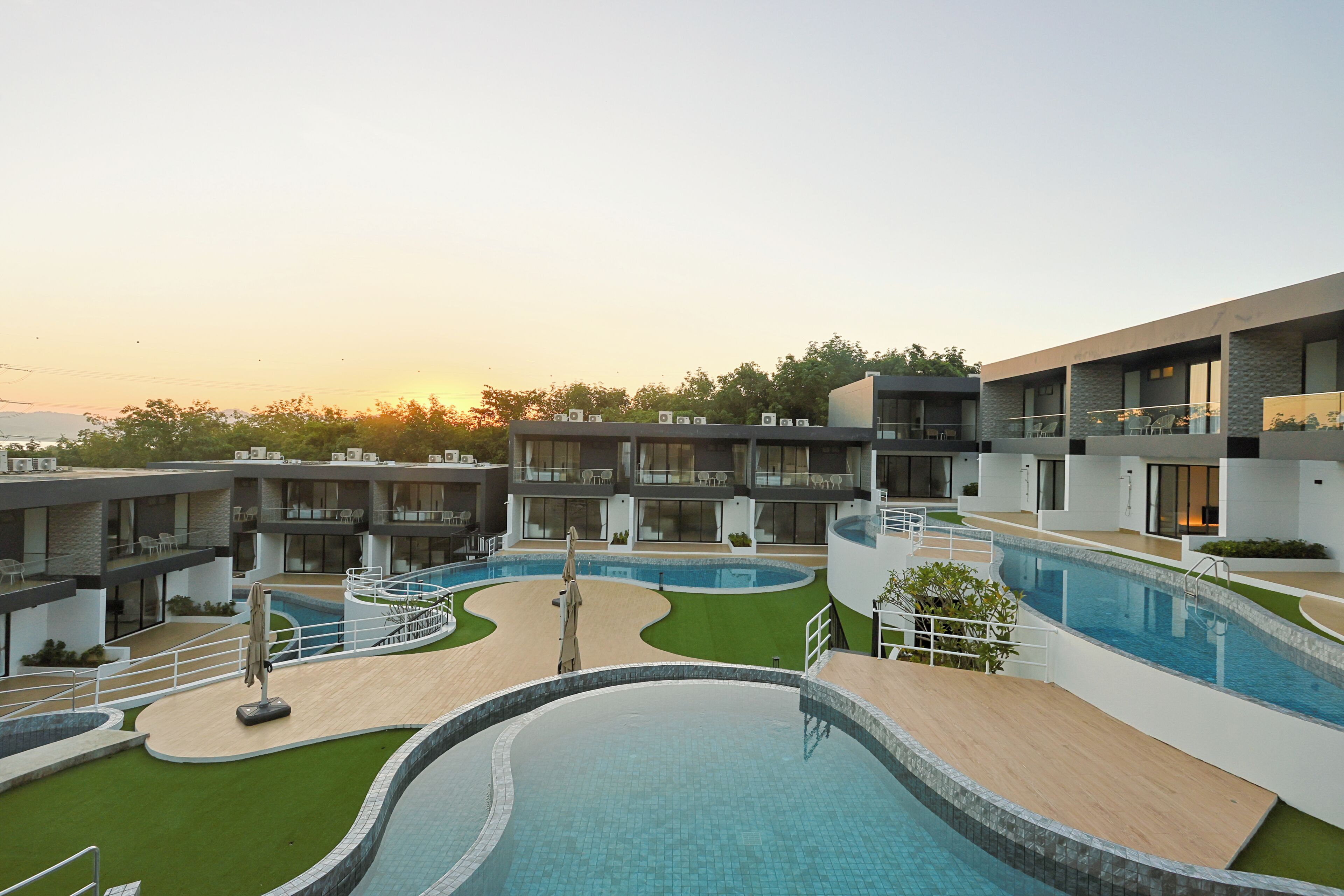 Un hotel moderno con diversi piani, piscine all'aperto e un giardino curato.