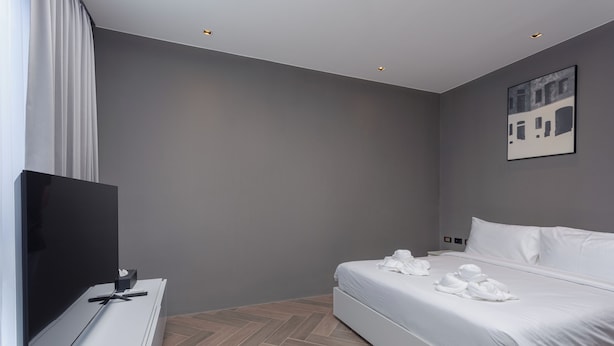 A modern hotel room with a bed, a flat-screen TV, a desk with a computer, and a herringbone-patterned floor.