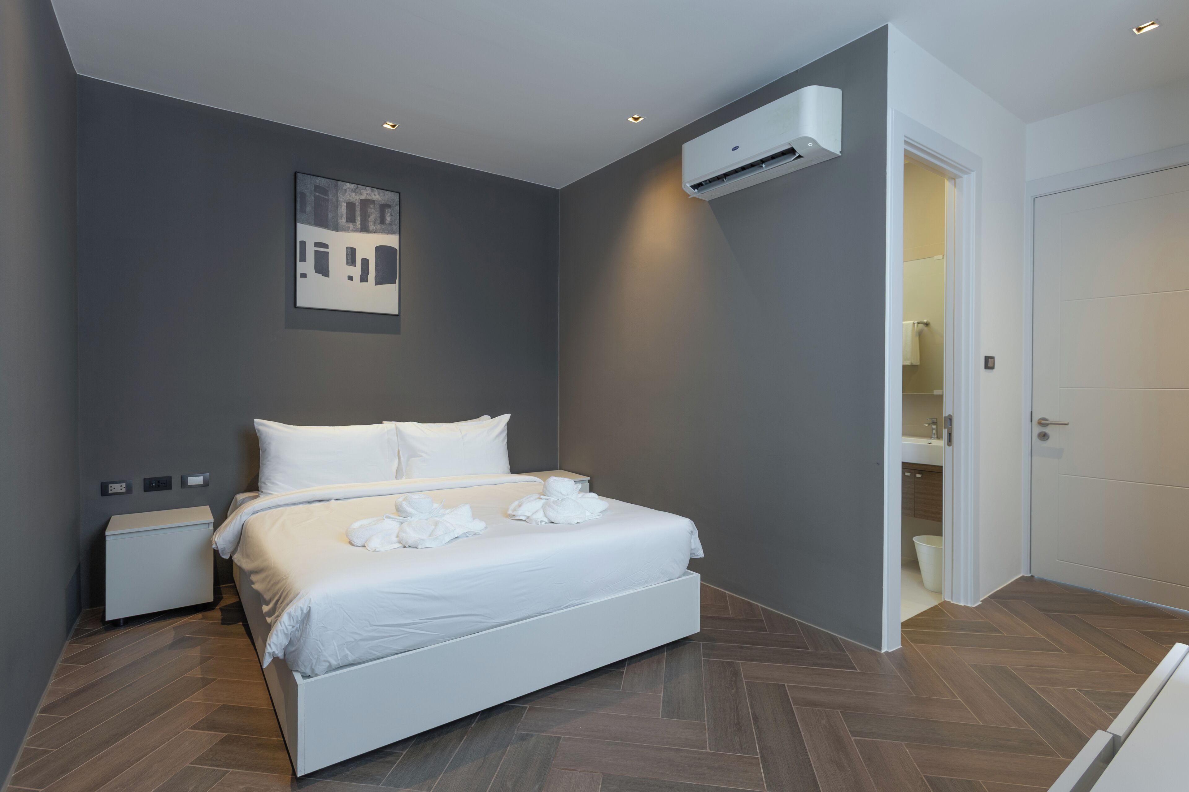 Een moderne hotelkamer met een groot bed, nachtkastje, airconditioning en een deur naar een badkamer.