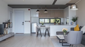 A modern kitchen with a central island, bar stools, and a dining area with a grey sofa and a coffee table.