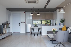 A modern kitchen with a central island, bar stools, and a dining area with a grey sofa and a coffee table. - Elite Suites Villas Maikhao Phuket (Thalang)
