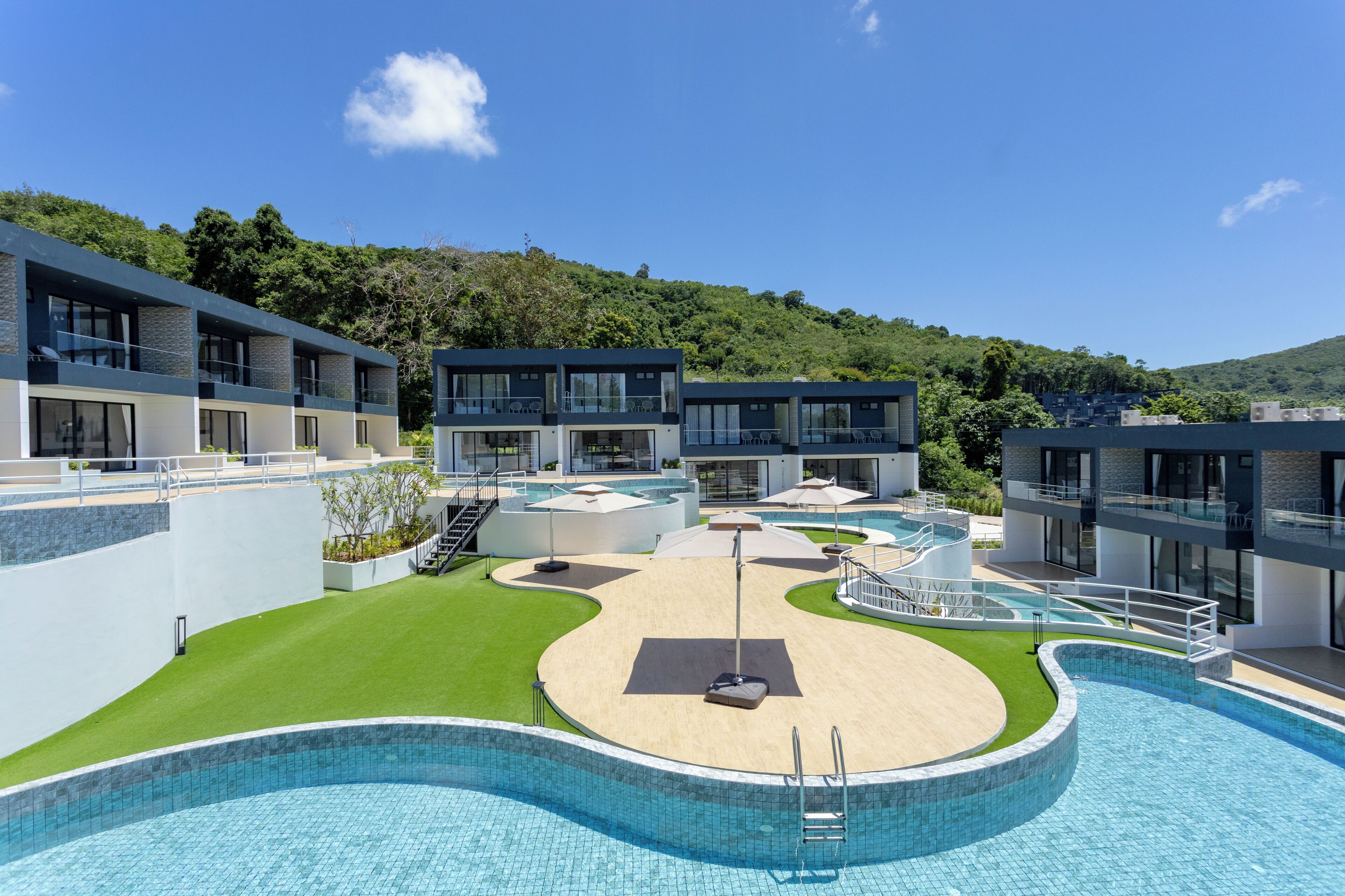 A modern hotel with a central swimming pool, multiple balconies, and a lush green landscape.