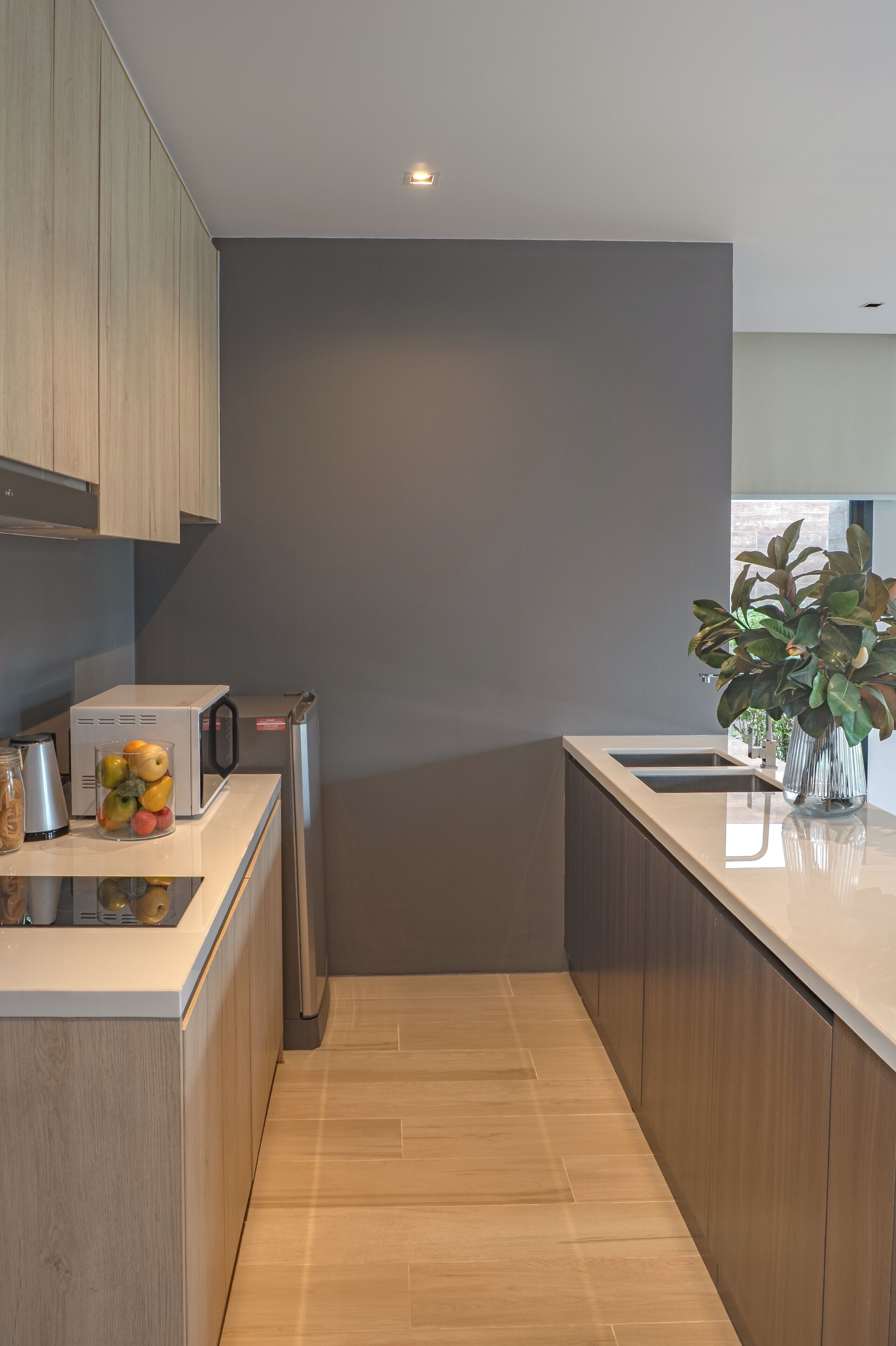 Una cocina moderna con armarios de madera, horno empotrado, lavamanos y una encimera con frutero y planta.