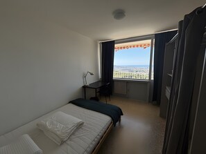 Ein Hotelzimmer mit Bett, Schreibtisch, Stuhl und einem Fenster mit Blick, sowie einem Vorhang.