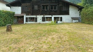 Un edificio de madera rústico con techo inclinado, un pequeño porche y vistas de una montaña boscosa.