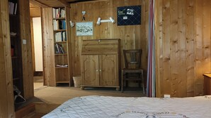 Una habitación de madera con una cama, una silla, un armario y una estantería.