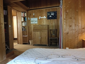 Ein Zimmer mit Holzboden, einem Bett, einem Sessel, einem Kleiderschrank und einem Bücherregal.