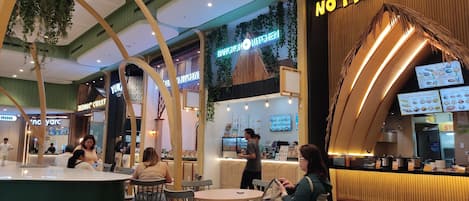 Un área de comedor interior con diversas disposiciones de asientos y una barra con una vitrina de menú.