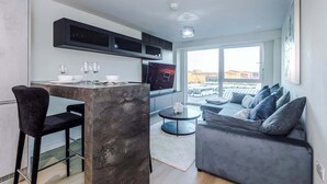 En moderne opholdsstue med et tekøkken, et spisebord med stole, en sofa og et fjernsyn.