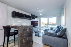 Ein zeitgemäßer Wohnraum mit Küchenbereich, einem Esstisch mit Stühlen, einer Couch und einem Fernseher.