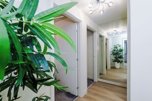 Ein Flur mit Pflanze, Tür und Spiegel, der eine Pflanze und eine Deckenleuchte reflektiert.